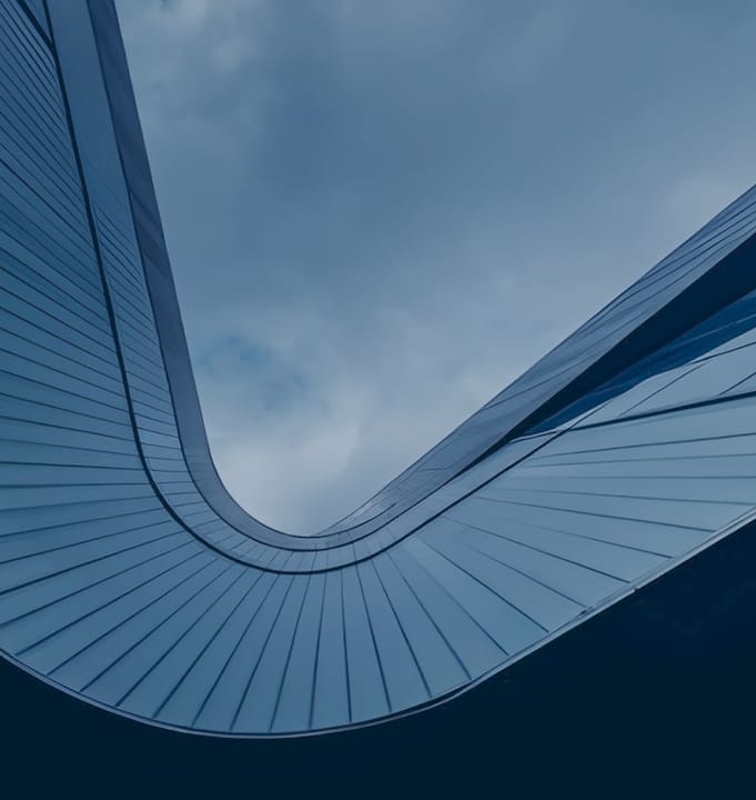 Close-up of a curved modern glass building architecture shot from below, symbolizing ambitious corporate vision, structural strength, and a company built to retain and grow its people